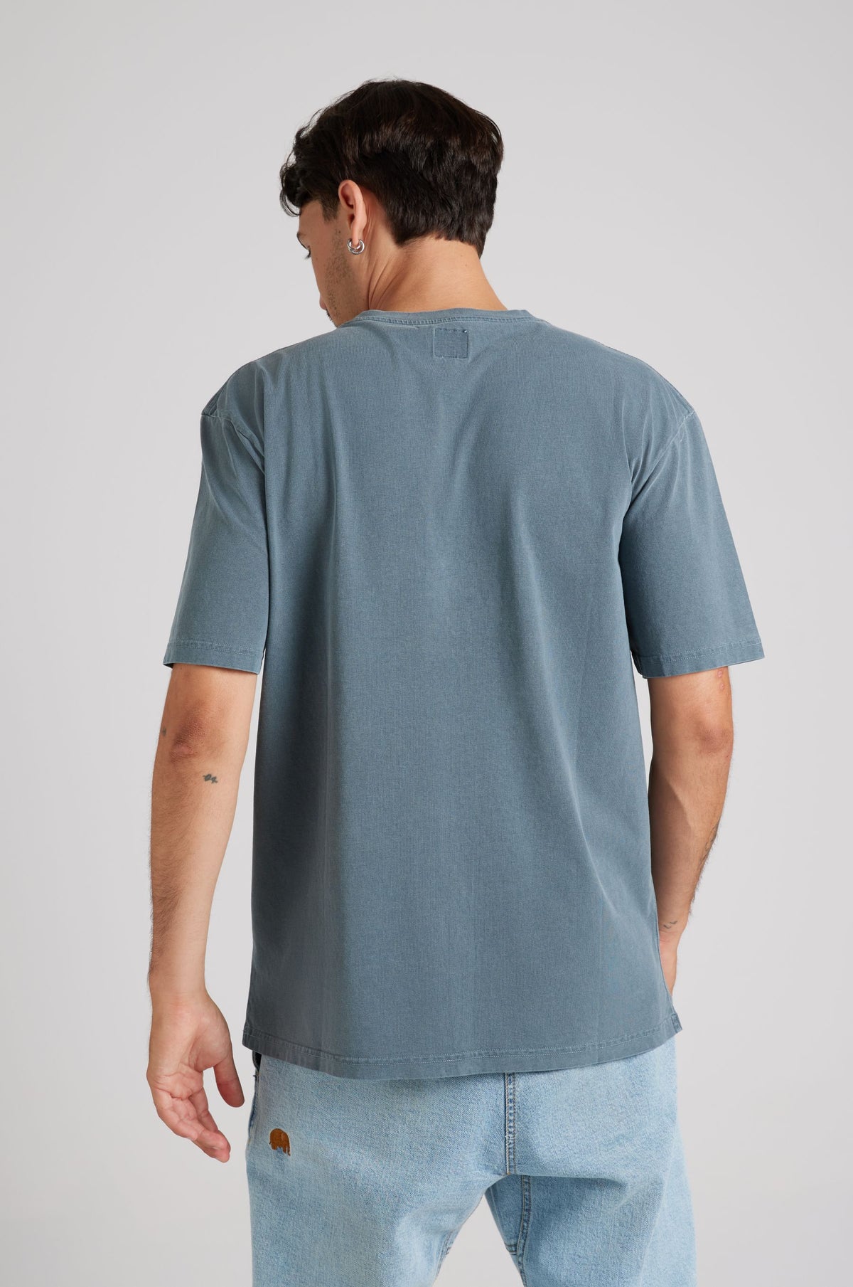 Personne portant un t-shirt Garza Pigment Dyed en Elm Green, vue de dos, associée à un jean en denim bleu clair. | TP_IMAGE_TYPE=MODEL_BACK