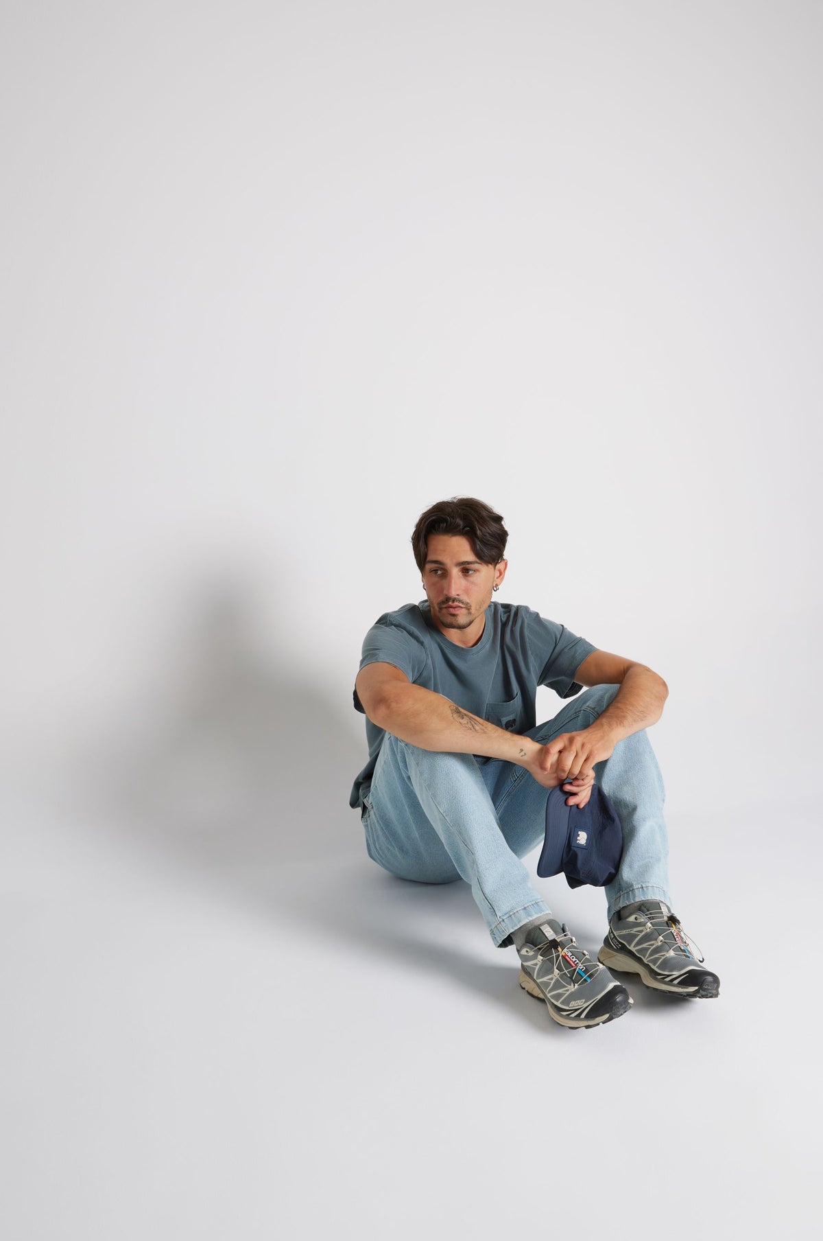 Personne portant un Garza Pigment Dyed T-Shirt en coloris Elm Green, assise au sol avec un jean et des chaussures. | TP_IMAGE_TYPE=MODEL_FRONT