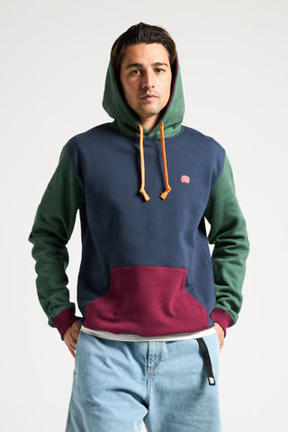 Persona che indossa una Organic Color Block Hoodie in blu, verde e bordeaux, con cappuccio e cordini arancioni, in posa su uno sfondo neutro | TP_IMAGE_TYPE=MODEL_FRONT