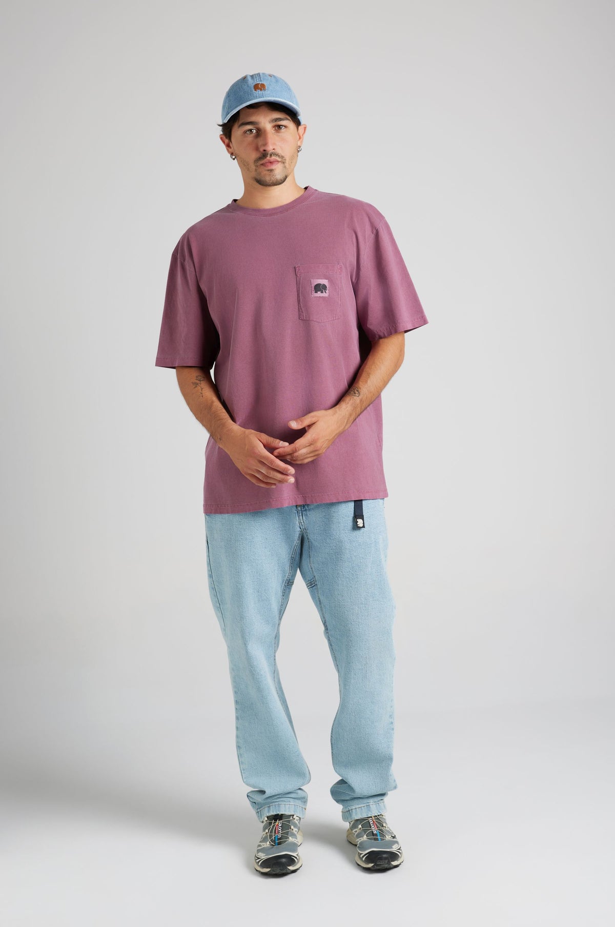 Persona che indossa una Garza Pigment Dyed T-Shirt in Garnacha Red abbinata a jeans azzurri e a un cappello in denim, in piedi davanti a uno sfondo neutro | TP_IMAGE_TYPE=MODEL_FRONT