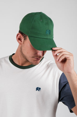 Persona che indossa un Musgo Green Logo Dad Cap, mentre sistema la visiera indossando una t-shirt chiara con scollo colorato. | TP_IMAGE_TYPE=MODEL_FRONT