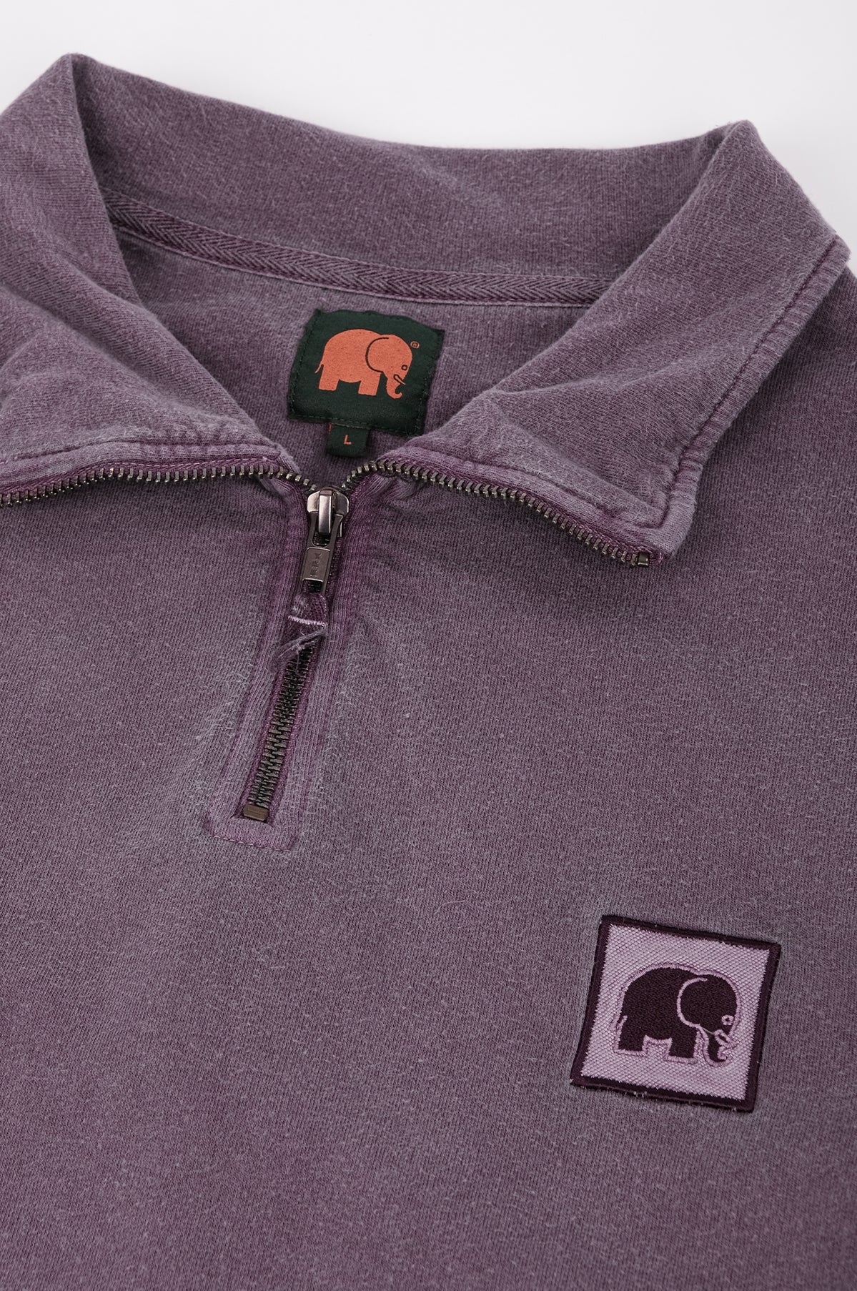 Dettaglio ravvicinato della felpa half zip Sauce Loopback Pigment Dyed in Sunset Purple, con colletto con zip e logo elefante. | TP_IMAGE_TYPE=DETAIL