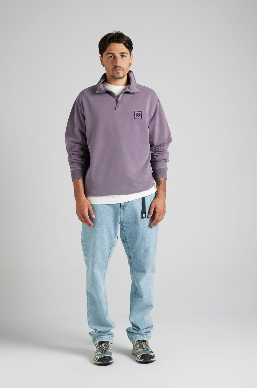 Persona che indossa una felpa half zip viola tramonto con un logo, abbinata a jeans azzurri | TP_IMAGE_TYPE=MODEL_FRONT