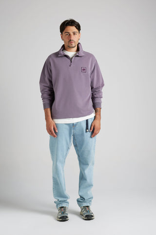 Persona che indossa una felpa half zip viola tramonto con un logo, abbinata a jeans azzurri | TP_IMAGE_TYPE=MODEL_FRONT