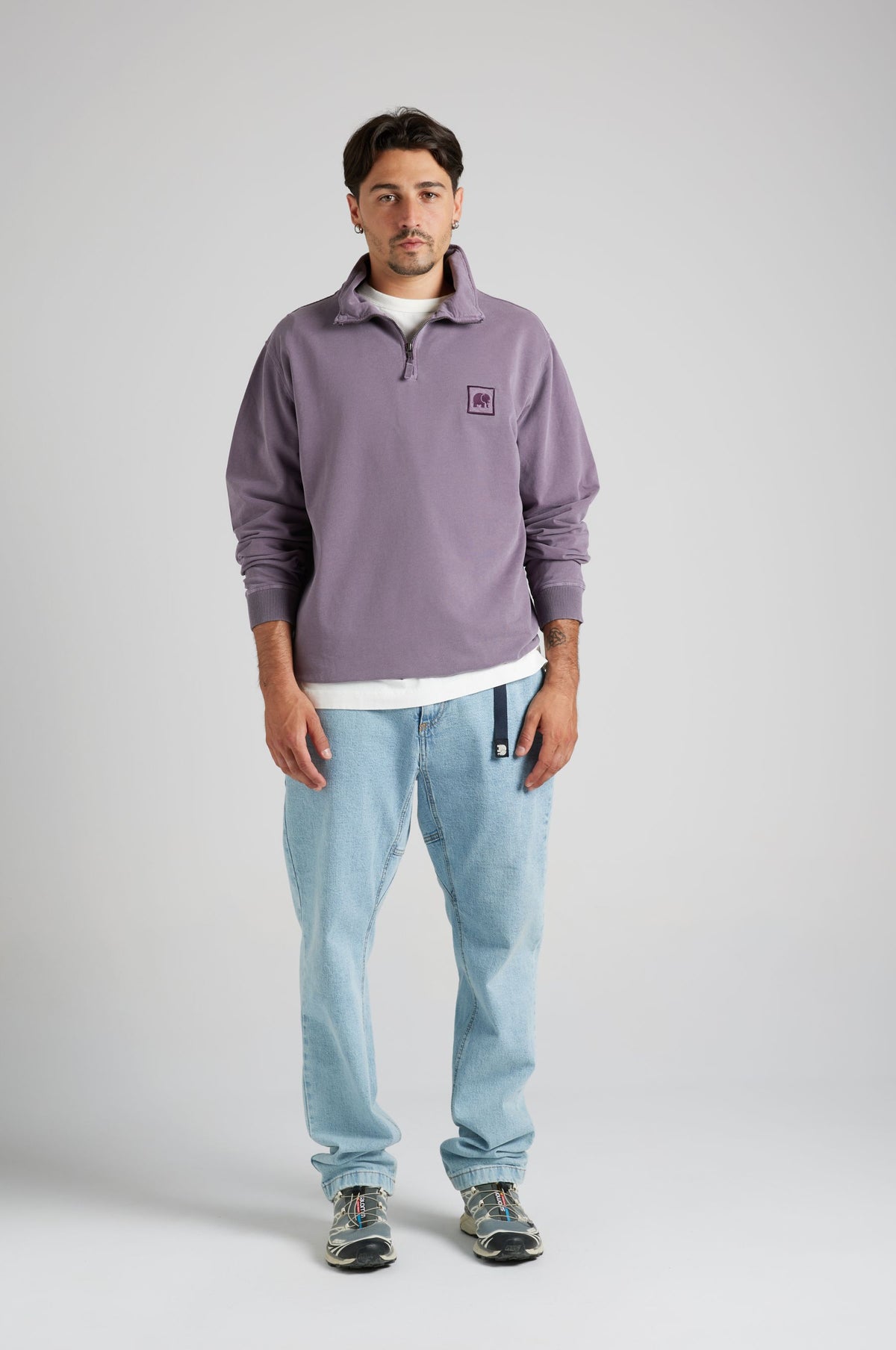 Persona che indossa una felpa half zip viola tramonto con un logo, abbinata a jeans azzurri | TP_IMAGE_TYPE=MODEL_FRONT