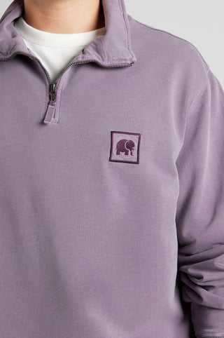 Persona che indossa una Sauce Loopback Pigment Dyed Half Zip Sweatshirt in Sunset Purple, con colletto con zip e una patch brandizzata sul petto. | TP_IMAGE_TYPE=MODEL_FRONT