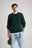Persona che indossa un maglione Tarbena Knit verde pino con vestibilità morbida e polsini a coste, con un cappello in mano | TP_IMAGE_TYPE=MODEL_FRONT