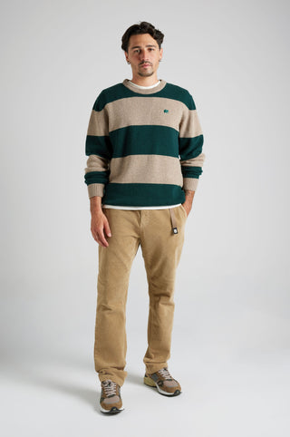 Persona che indossa una Sella Knit a righe in Pine Green e Nomad Brown, abbinata a pantaloni in velluto a coste, in posa su uno sfondo neutro. | TP_IMAGE_TYPE=MODEL_FRONT