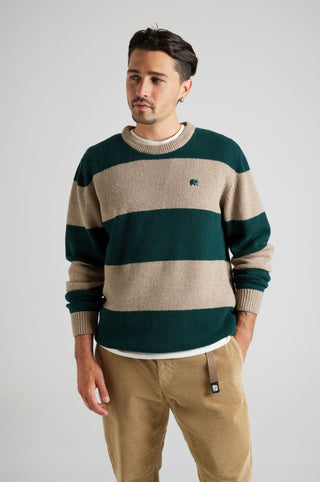 Persona che indossa un maglione Sella Knit in pine green e nomad brown, con righe e logo ricamato, abbinato a pantaloni in velluto a coste beige. | TP_IMAGE_TYPE=MODEL_FRONT