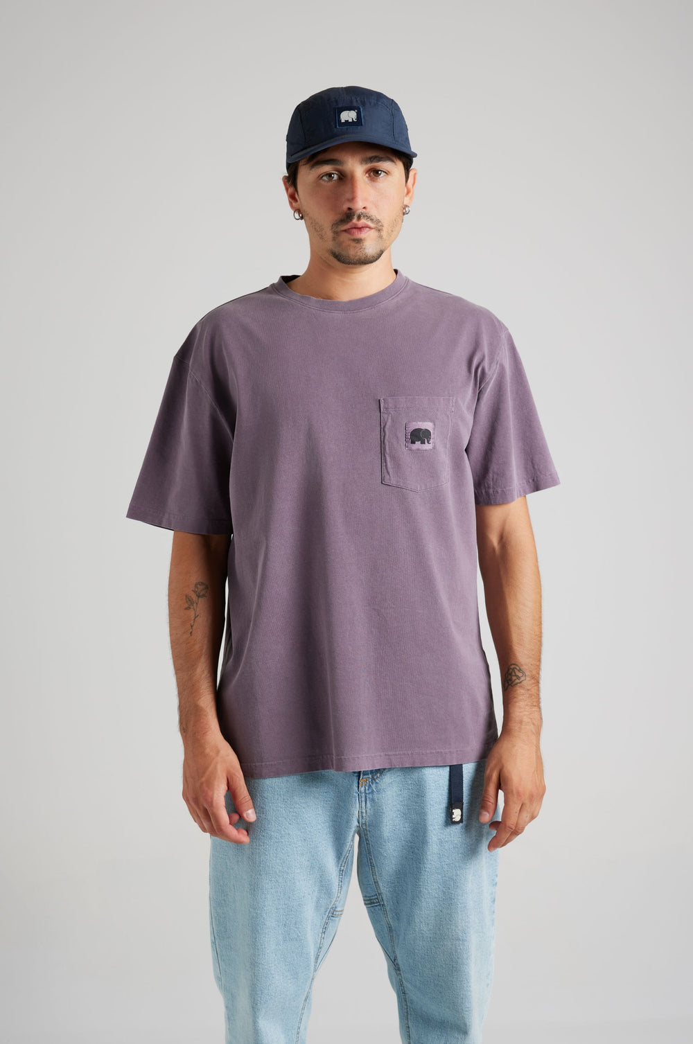Persona che indossa una Garza Pigment Dyed T-Shirt in Sunset Purple con tasca frontale, abbinata a pantaloni in denim chiaro e un cappellino blu navy | TP_IMAGE_TYPE=MODEL_FRONT