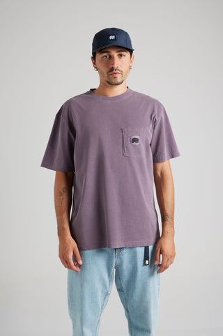 Persona che indossa una Garza Pigment Dyed T-Shirt in Sunset Purple con tasca frontale, abbinata a pantaloni in denim chiaro e un cappellino blu navy | TP_IMAGE_TYPE=MODEL_FRONT