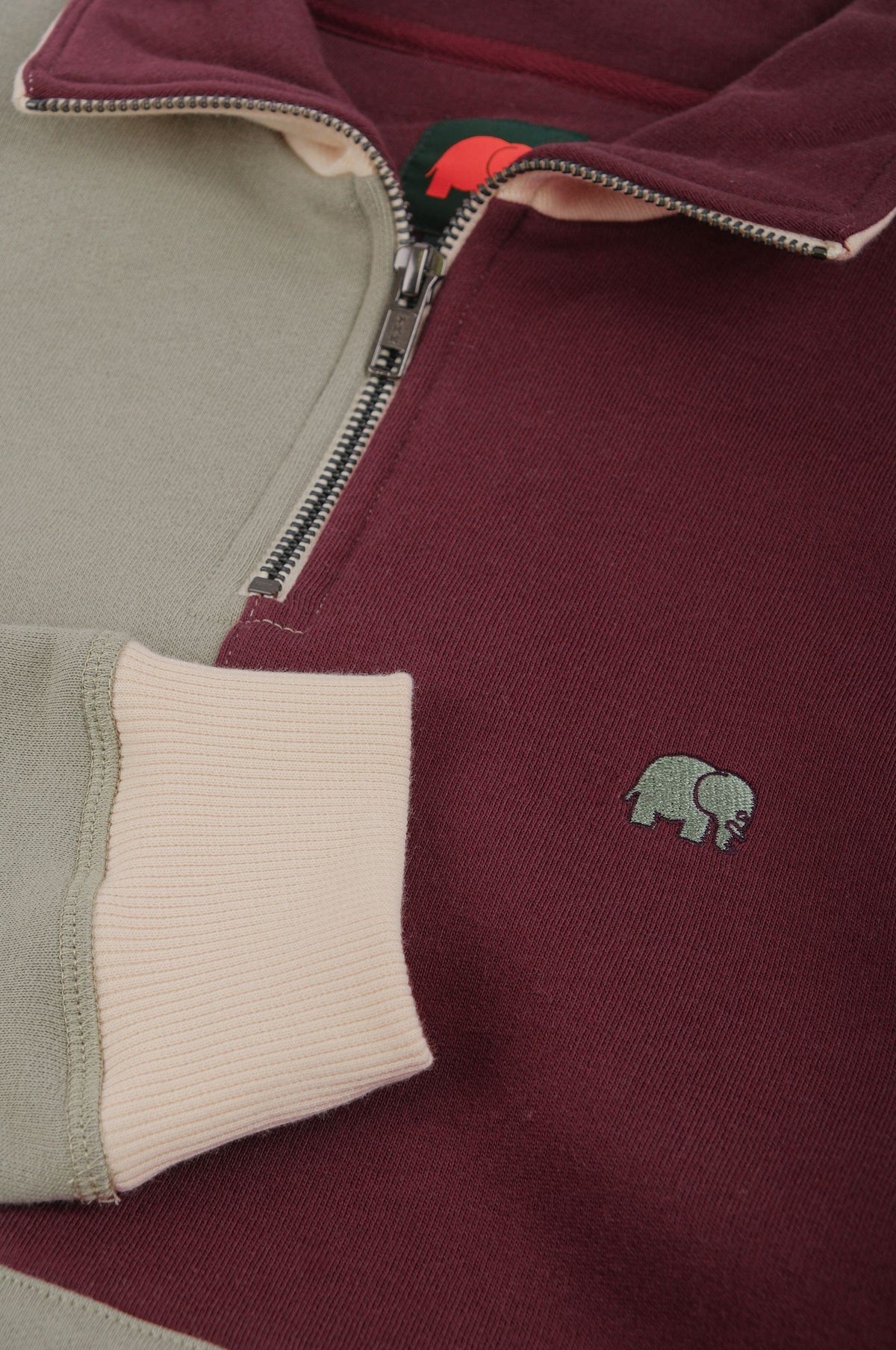 Dettaglio ravvicinato della Color Block Quarter Zip Sweatshirt in Iron Veil, con i blocchi di colore bordeaux e verde, la zip e il logo elefante ricamato. | TP_IMAGE_TYPE=DETAIL