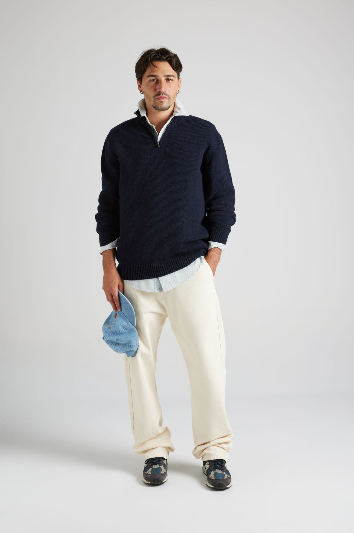 Personne portant le Bernia Quarter Zip Knit en Ocean Blue, associé à un pantalon de couleur claire et tenant une casquette bleue | TP_IMAGE_TYPE=MODEL_FRONT
