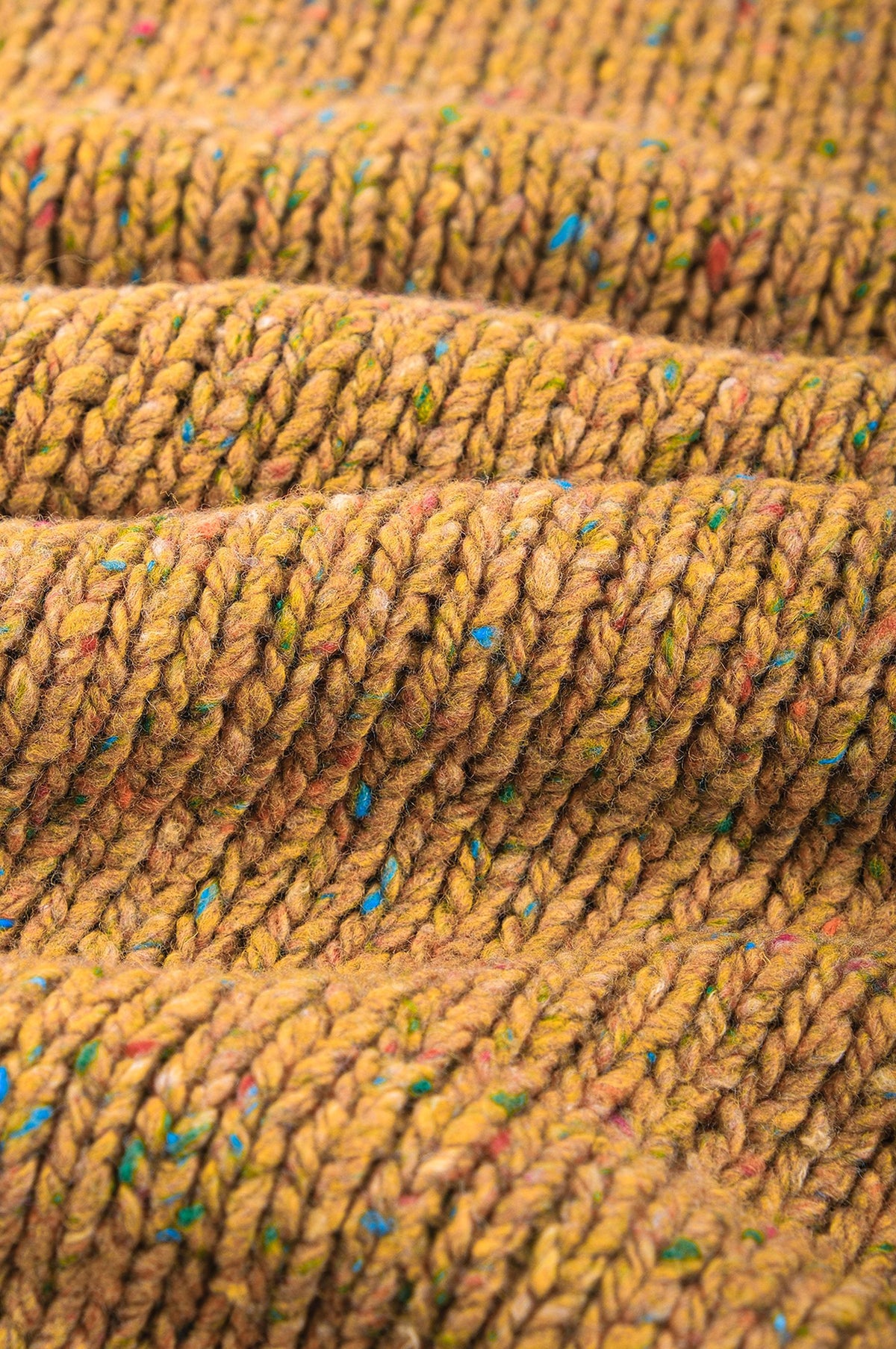 Close-up detail of the textured knit pattern of the Maigmo Knit Dijon, showcasing its vibrant hues and color flecks. | TP_IMAGE_TYPE=DETAIL
