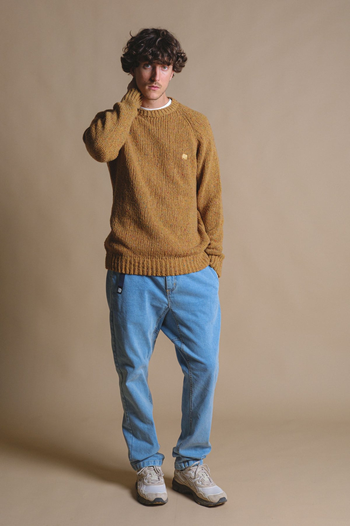 Person wearing a Maigmo Knit Dijon sweater styled with loose jeans and sneakers, looking thoughtfully at the camera against a soft, neutral background. | TP_IMAGE_TYPE=MODEL_FRONT