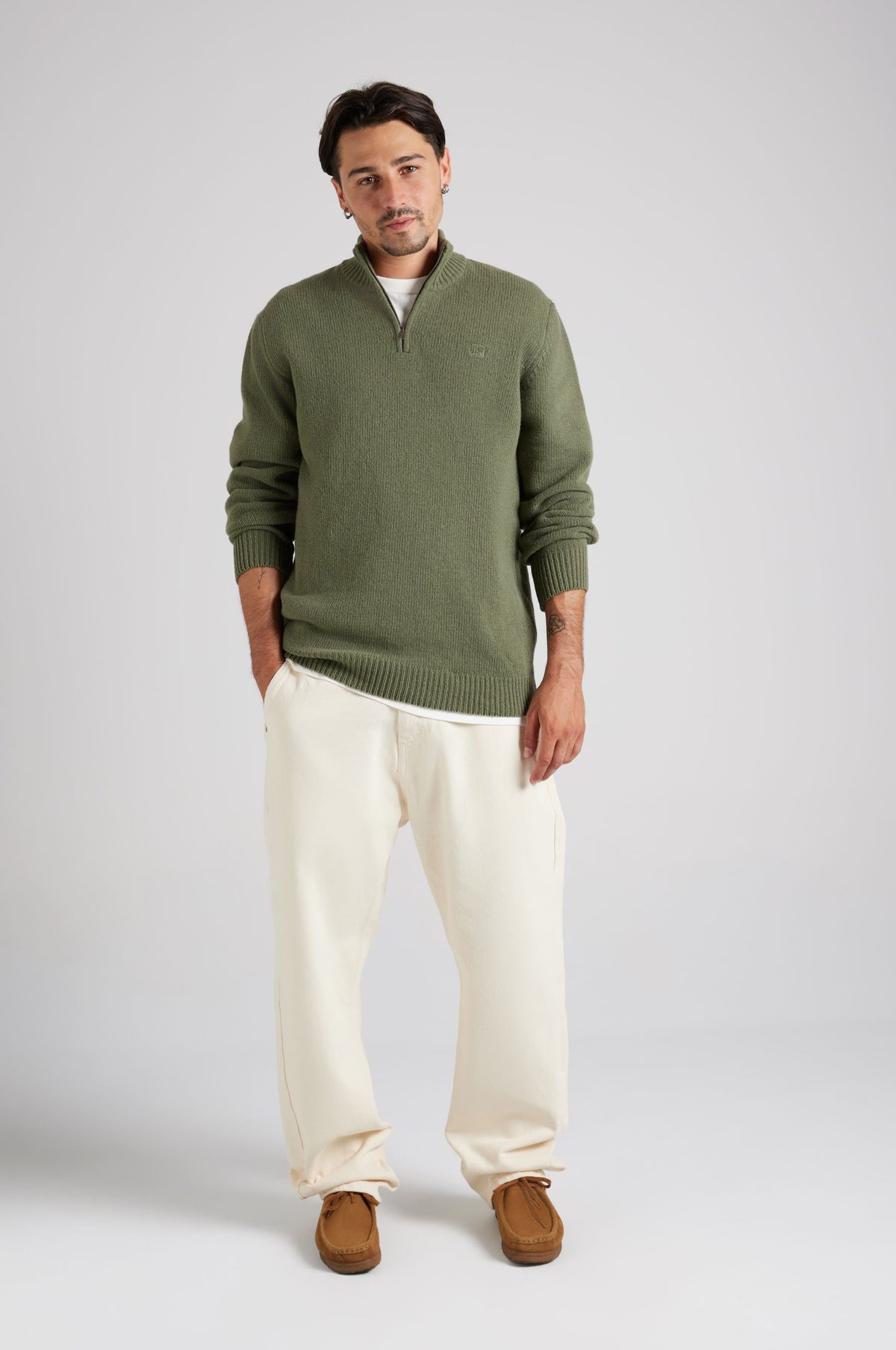 Personne portant un Bernia Quarter Zip Knit en Sage, stylisée avec un pantalon crème et des mocassins marron, debout avec assurance, les mains dans les poches | TP_IMAGE_TYPE=MODEL_FRONT