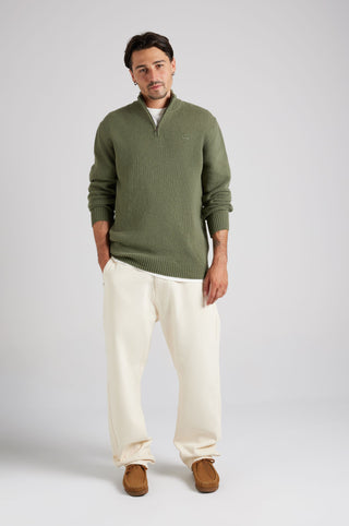 Personne portant un Bernia Quarter Zip Knit en Sage, stylisée avec un pantalon crème et des mocassins marron, debout avec assurance, les mains dans les poches | TP_IMAGE_TYPE=MODEL_FRONT