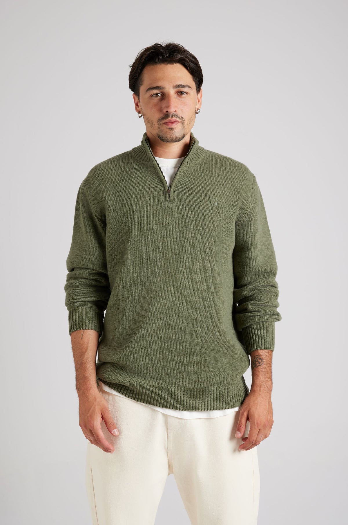 Personne portant le Bernia Quarter Zip Knit en Sage, avec une fermeture à demi-zip élégante et une finition texturée, associé à un pantalon clair. | TP_IMAGE_TYPE=MODEL_FRONT
