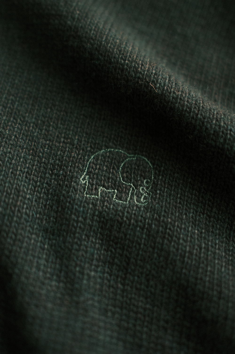 Dettaglio ravvicinato del Tarbena Knit in Pine Green che mostra lo scollo a coste e il logo dell'elefante. | TP_IMAGE_TYPE=DETAIL