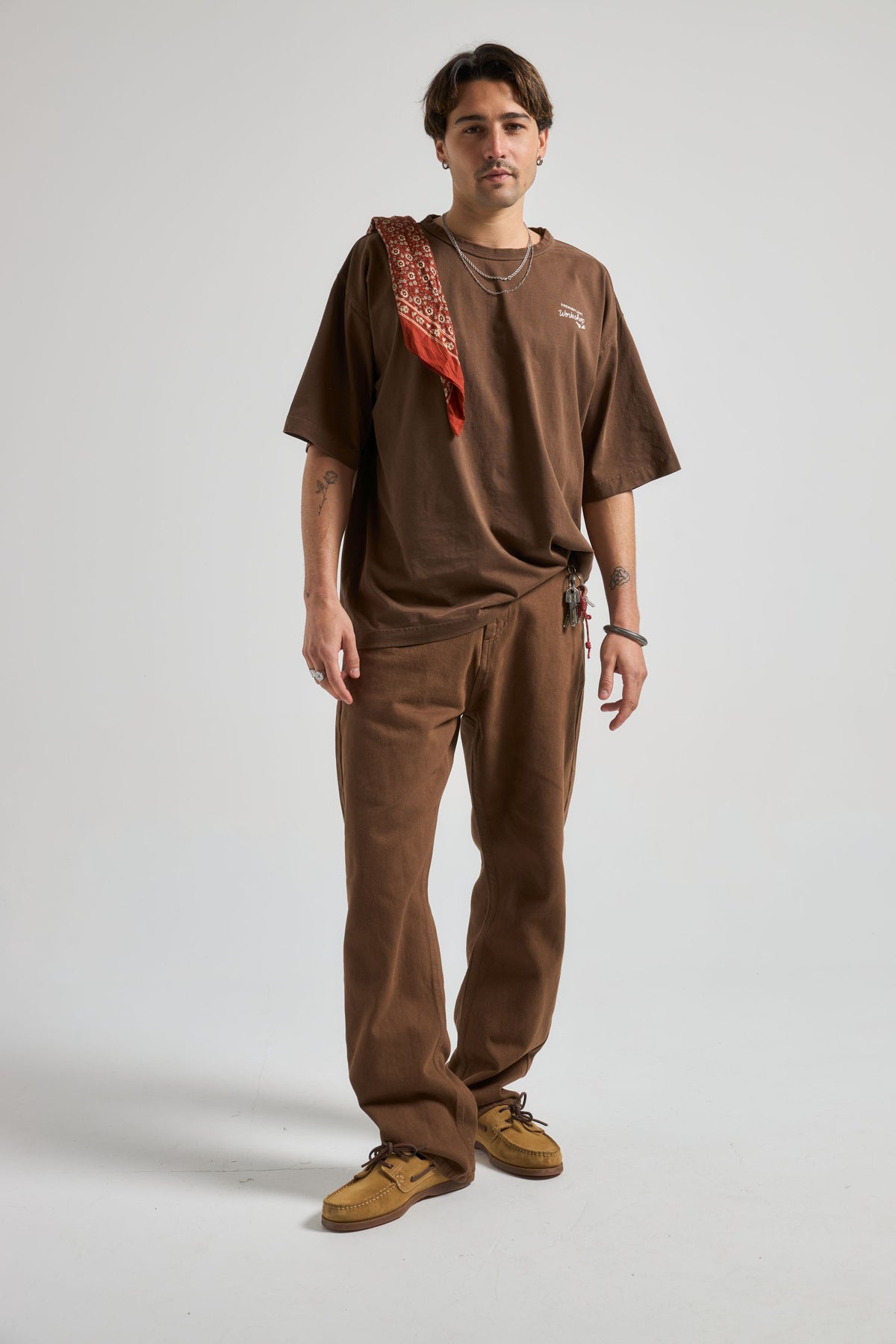 Persona che indossa Operator Pants in Saddle Brown abbinati a una t-shirt marrone e accessori, in piedi in un ambiente neutro. | TP_IMAGE_TYPE=MODEL_FRONT