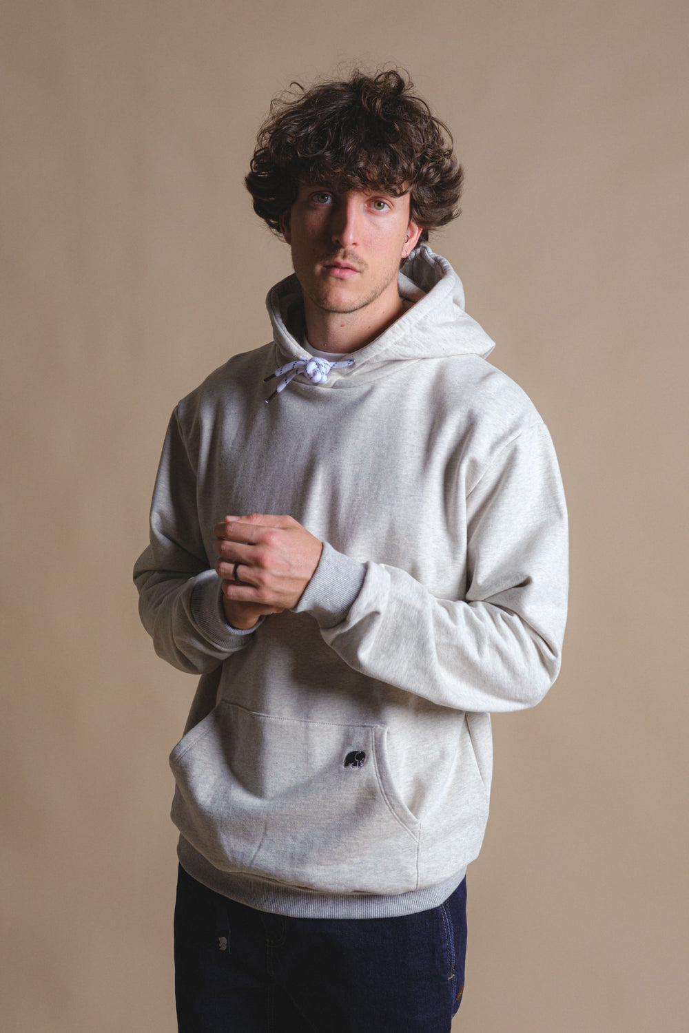 Persona che indossa una felpa con cappuccio in pile reversibile in grigio mélange caldo, in piedi con le mani giunte davanti a uno sfondo neutro. | TP_IMAGE_TYPE=MODEL_FRONT