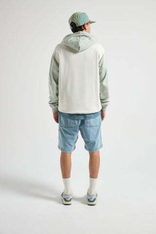 Personne portant un sweat à capuche gris clair, un short en jean et une casquette sur fond blanc