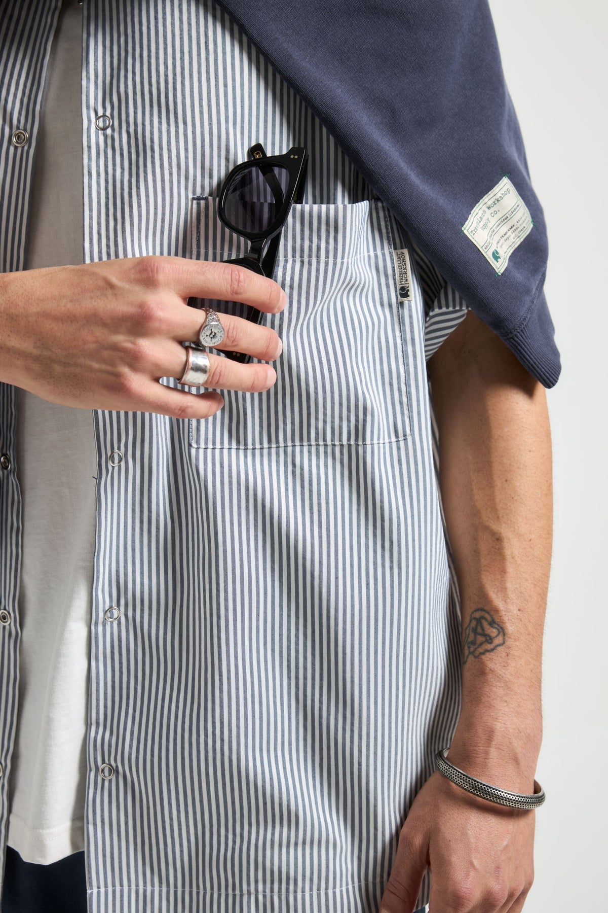 Persona che indossa una Mechanic Box Seaqual®Yarn S/S Shirt in Indigo Stripes, tiene in mano gli occhiali da sole e mostra un outfit stiloso | TP_IMAGE_TYPE=MODEL_FRONT