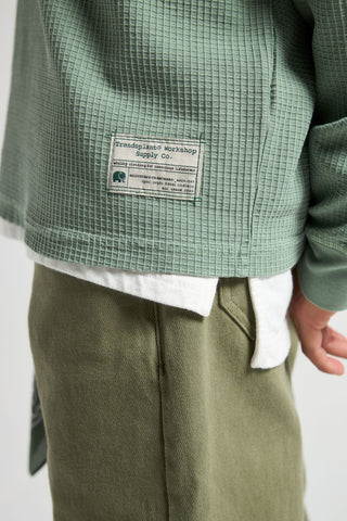 Personne portant une chemise henley en maille gaufrée verte Hedge, vue de dos, avec un maillot de corps blanc et un pantalon vert olive | TP_IMAGE_TYPE=MODEL_BACK