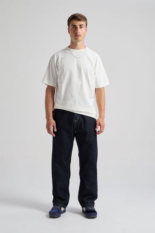 Personne portant le pantalon Operator Relaxed en denim foncé, associé à une chemise blanche et des baskets, debout devant un fond neutre. | TP_IMAGE_TYPE=MODEL_FRONT