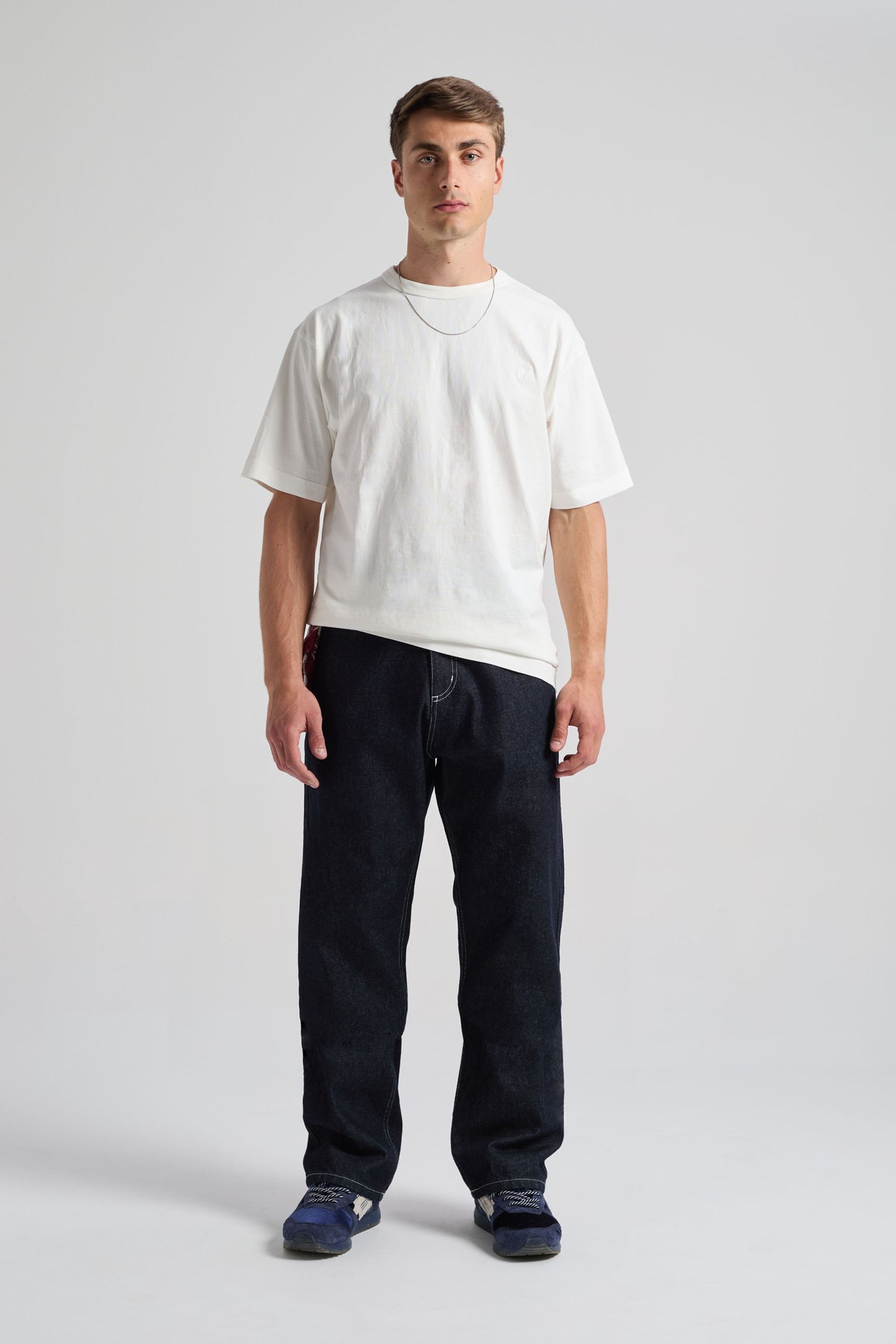 Personne portant le pantalon Operator Relaxed en denim foncé, associé à une chemise blanche et des baskets, debout devant un fond neutre. | TP_IMAGE_TYPE=MODEL_FRONT