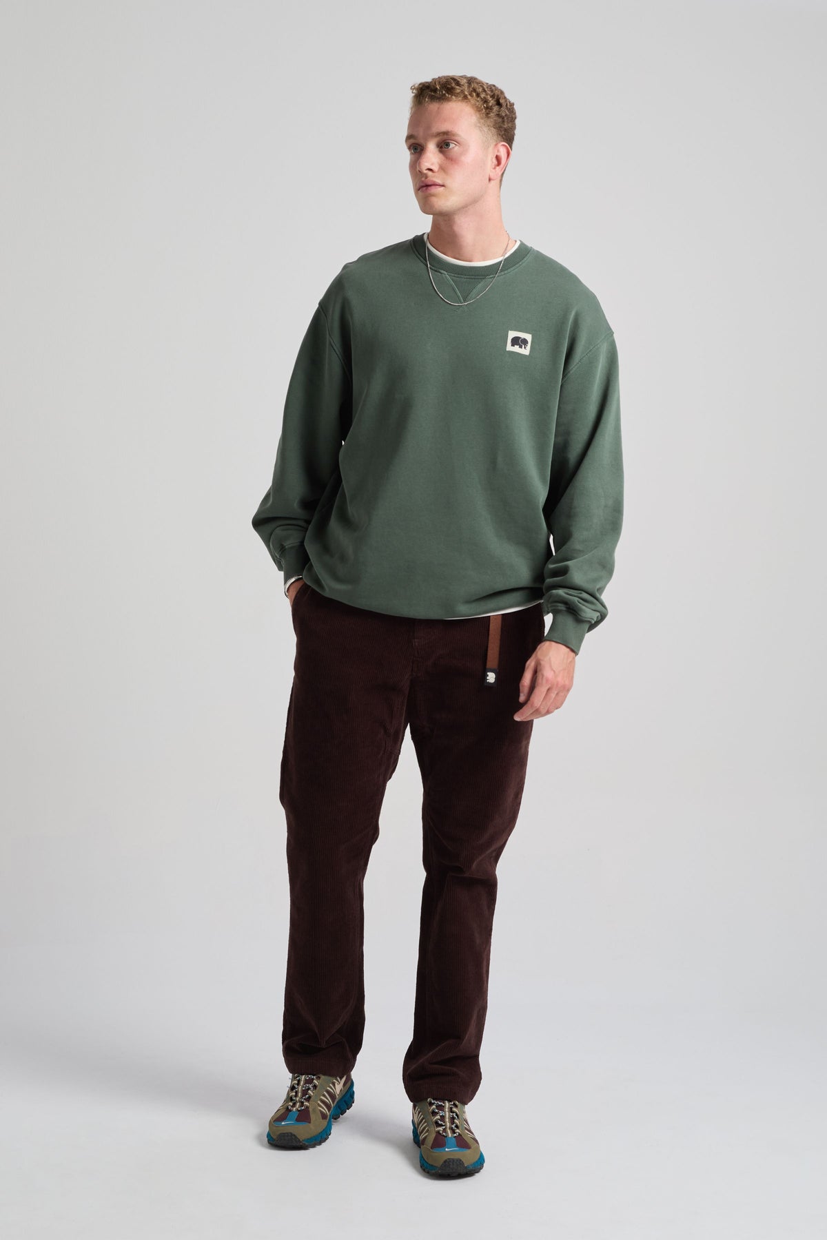 Personne portant le Corduroy Ecodye Climber Pant en Chicory Coffee, associé à un sweat-shirt vert et à des accessoires | TP_IMAGE_TYPE=MODEL_FRONT