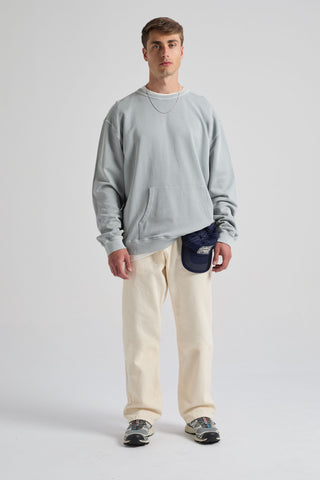 Persona che indossa una felpa Hangar Sweatshirt Quarry Blue con tasca frontale, abbinata a pantaloni chiari e a un cappellino | TP_IMAGE_TYPE=MODEL_FRONT