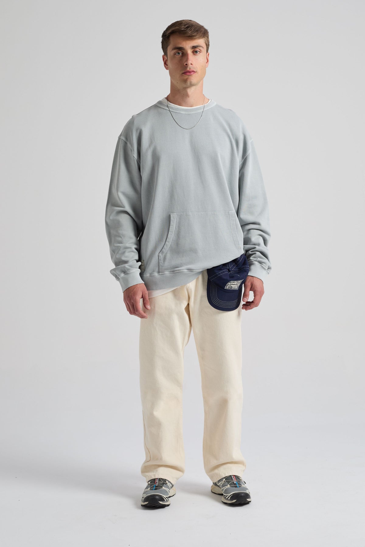Persona che indossa una felpa Hangar Sweatshirt Quarry Blue con tasca frontale, abbinata a pantaloni chiari e a un cappellino | TP_IMAGE_TYPE=MODEL_FRONT