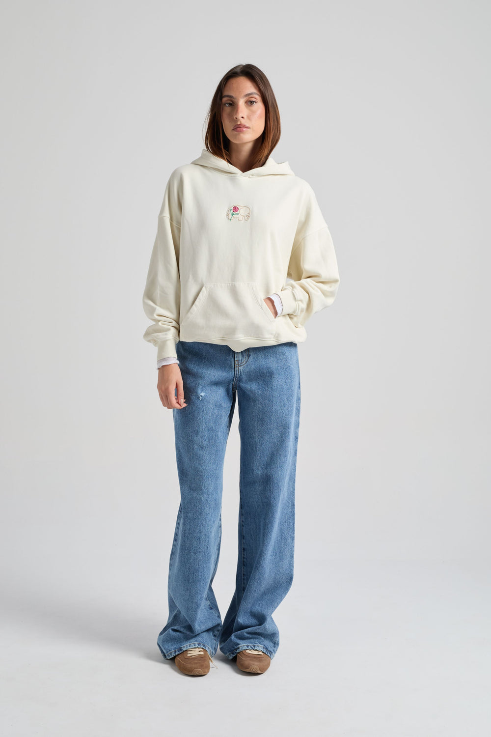 Persona che indossa una felpa da donna bianco antico con una grafica sul petto, abbinata a jeans azzurri e scarpe marroni, in piedi davanti a uno sfondo neutro. | TP_IMAGE_TYPE=MODEL_FRONT