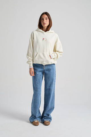 Persona che indossa una felpa da donna bianco antico con una grafica sul petto, abbinata a jeans azzurri e scarpe marroni, in piedi davanti a uno sfondo neutro. | TP_IMAGE_TYPE=MODEL_FRONT