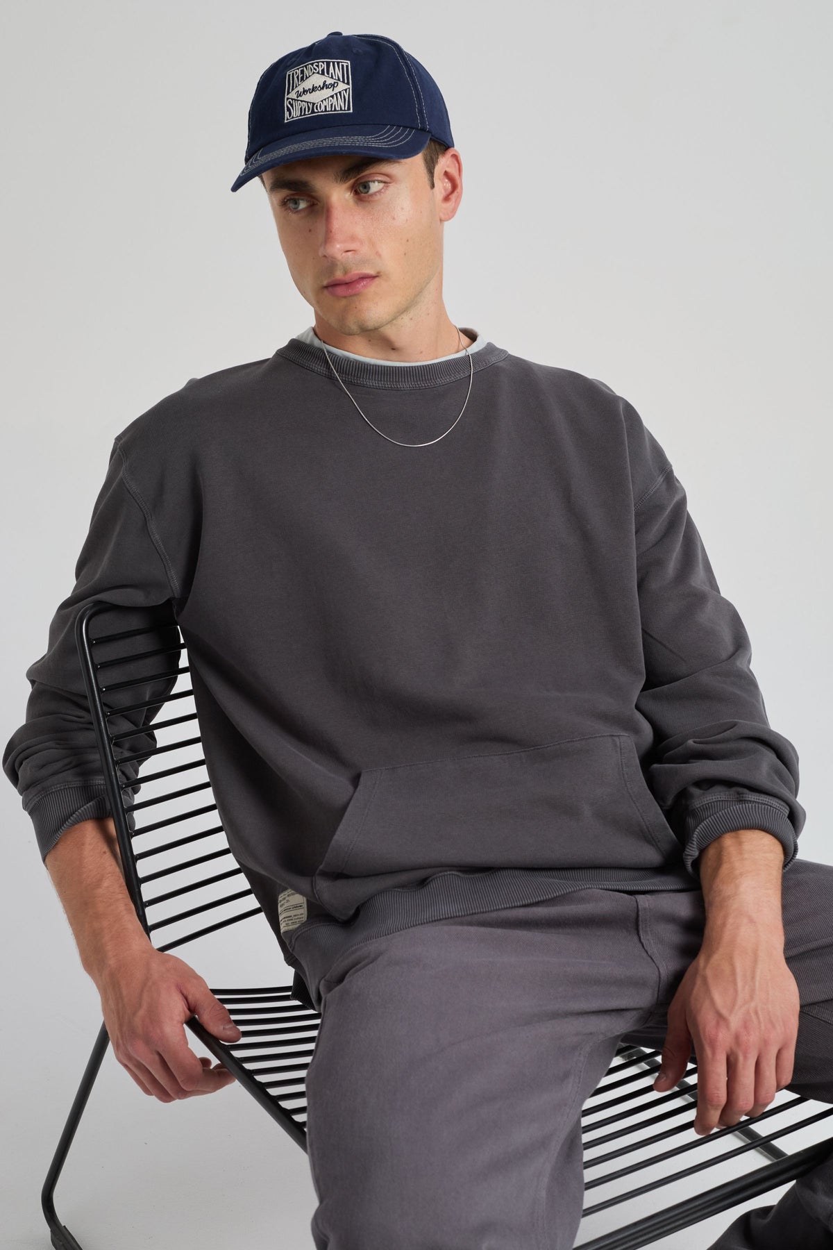 Personne portant le Factory Oversized Sweatshirt Forged Iron, assise nonchalamment sur une chaise moderne. | TP_IMAGE_TYPE=MODEL_FRONT