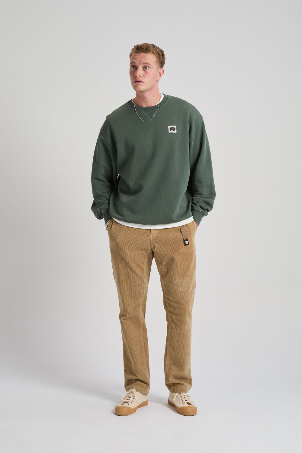 Persona che indossa una felpa verde e pantaloni marroni su sfondo bianco. TP_IMAGE_TYPE=MODEL_FRONT