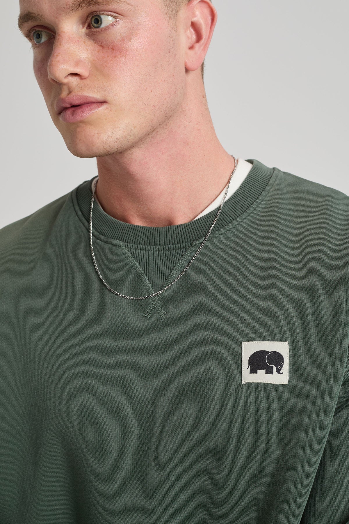 Persona che indossa un maglione verde con un piccolo logo su uno sfondo neutro. TP_IMAGE_TYPE=MODEL_FRONT