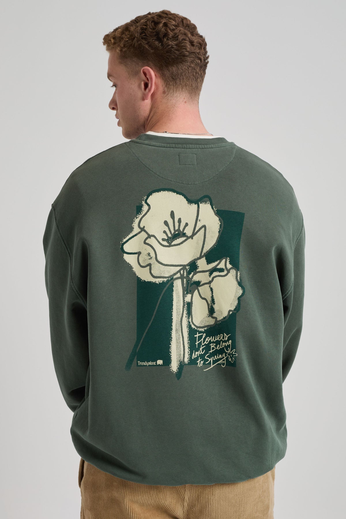 Persona che indossa una felpa verde con motivo floreale sulla schiena su sfondo neutro. TP_IMAGE_TYPE=MODEL_BACK