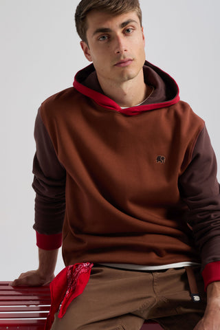 Persona che indossa una felpa Color Block in Cherry Mahogany con cappuccio rosso e corpo marrone, abbinata a una bandana rossa in vita. | TP_IMAGE_TYPE=MODEL_FRONT
