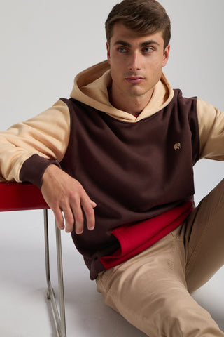 Personne portant un sweat à capuche color block en Solemnity Brown avec une capuche crème contrastante, assise sur le sol avec un t-shirt rouge en dessous et un pantalon kaki | TP_IMAGE_TYPE=MODEL_FRONT