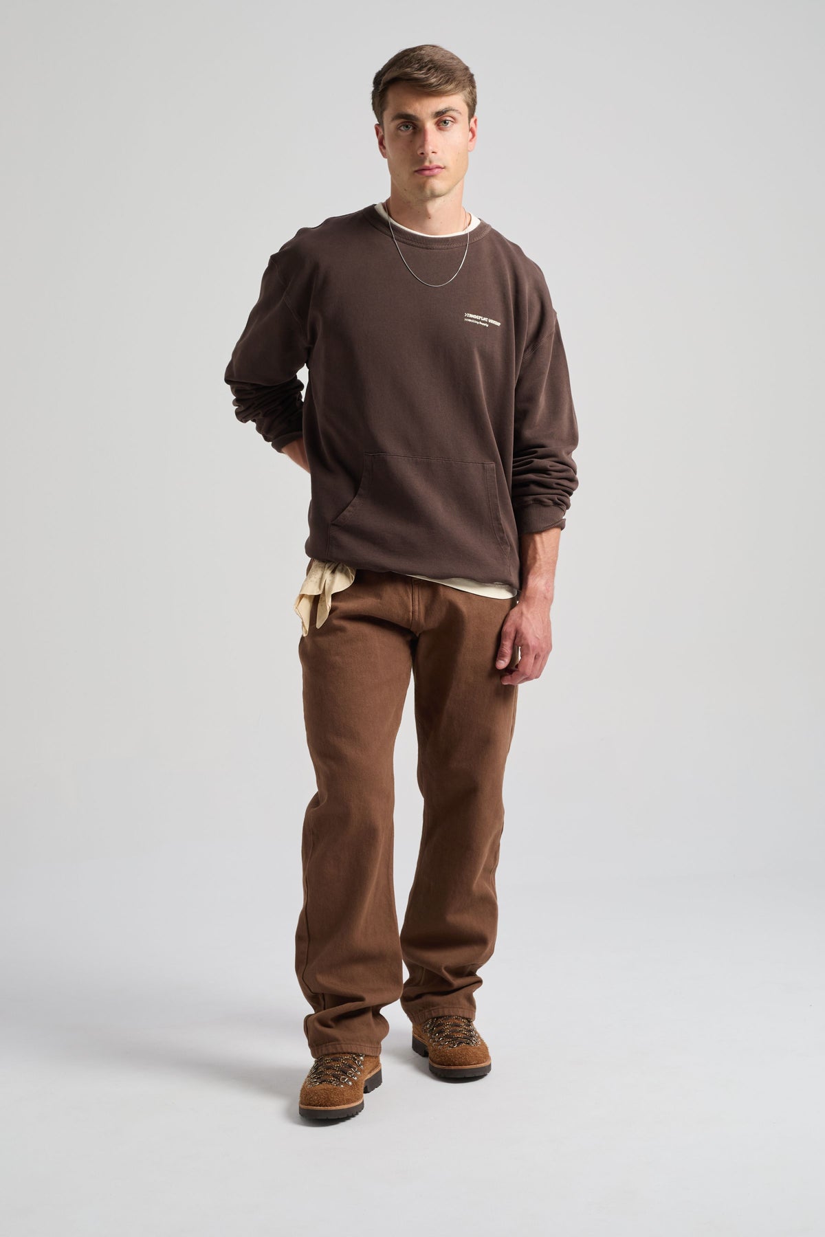 Personne portant un Core Oversized Sweatshirt couleur Coffee Bean, associé à un pantalon marron et des accessoires, debout sur un fond neutre. | TP_IMAGE_TYPE=MODEL_FRONT