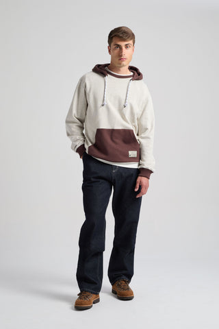 Persona che indossa la Hooded Oversized Sweatshirt in Warm Heather Grey/Coffee, caratterizzata da un design bicolore con cappuccio e tasca frontale, abbinata a jeans scuri e scarpe casual | TP_IMAGE_TYPE=MODEL_FRONT