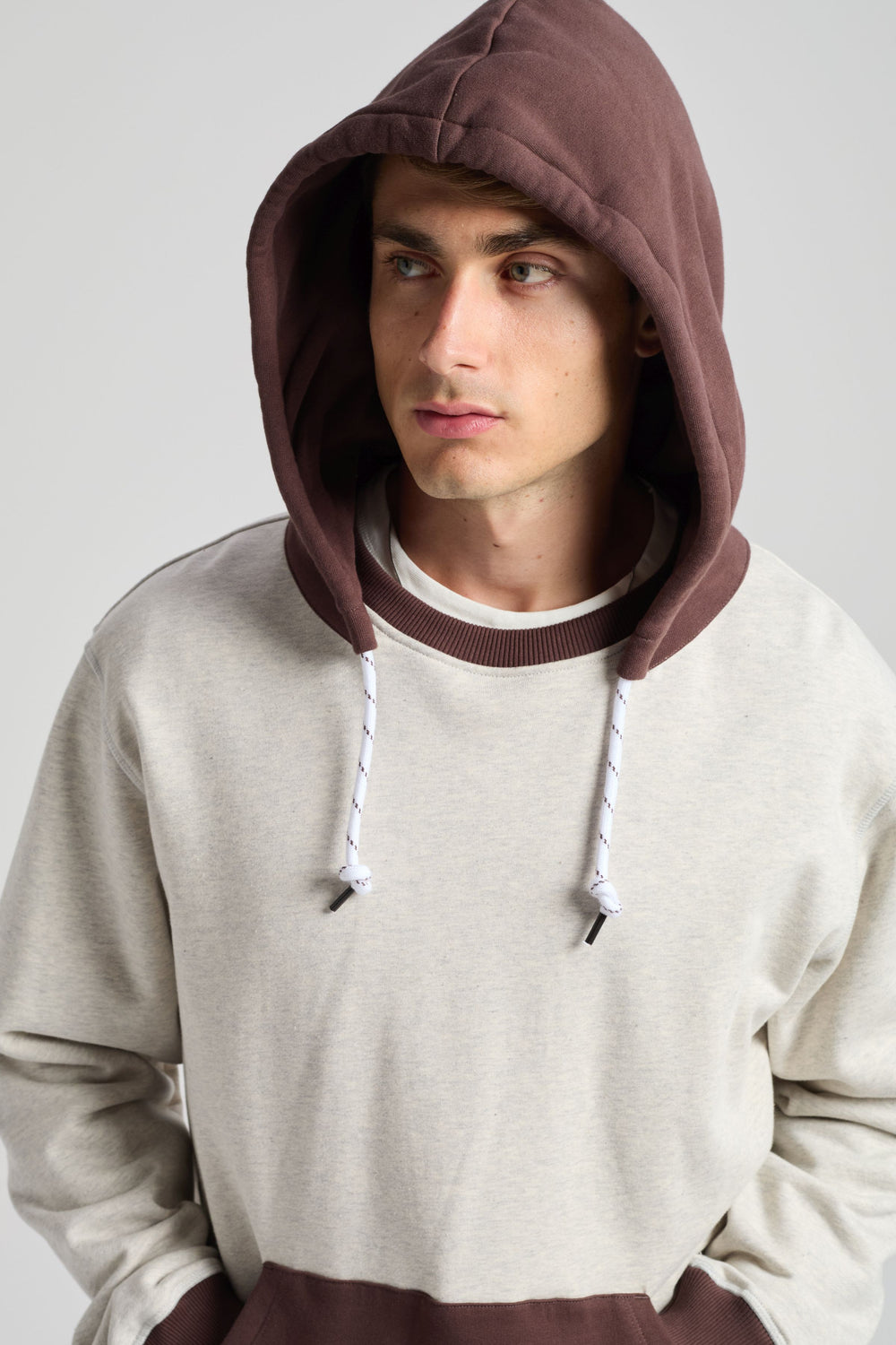 Persona che indossa The Hooded Oversized Sweatshirt in grigio mélange caldo e coffee, con cappuccio accogliente e orlo a contrasto | TP_IMAGE_TYPE=MODEL_FRONT