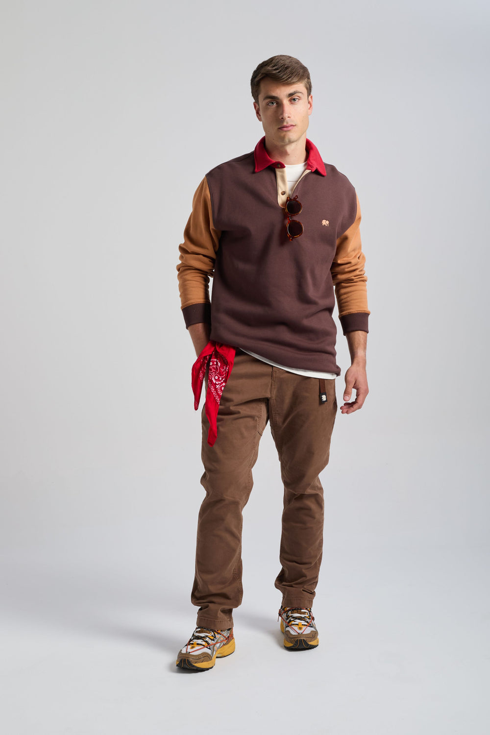 Persona che indossa una felpa polo Color Block in Solemnity Brown con colletto rosso, abbinata a pantaloni beige e sneakers, in posa sicura in uno studio fotografico. | TP_IMAGE_TYPE=MODEL_FRONT