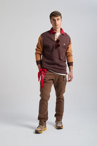 Persona che indossa una felpa polo Color Block in Solemnity Brown con colletto rosso, abbinata a pantaloni beige e sneakers, in posa sicura in uno studio fotografico. | TP_IMAGE_TYPE=MODEL_FRONT