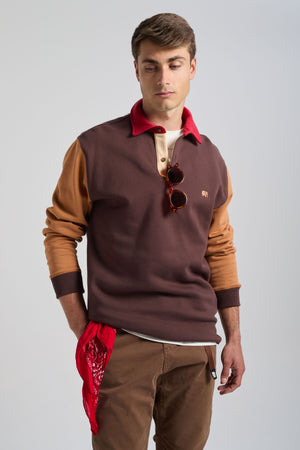 Persona che indossa una Color Block Polo Sweatshirt in Solemnity Brown con collo rosso, abbinata a pantaloni marroni e con una bandana rossa in mano. | TP_IMAGE_TYPE=MODEL_FRONT
