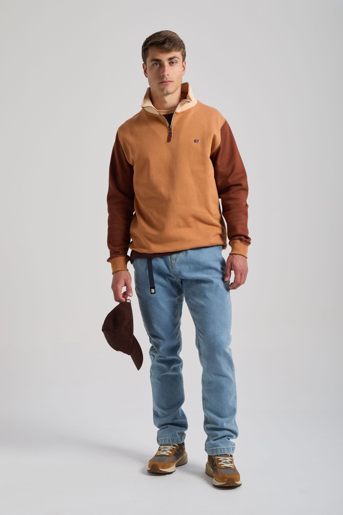 Personne portant un sweat à demi-zip color block en coloris Cashew avec des manches contrastantes et tenant une casquette marron | TP_IMAGE_TYPE=MODEL_FRONT