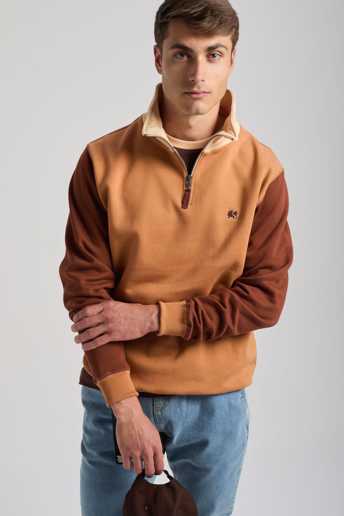 Personne portant un sweat à demi-zip à color block en cashew et marron, tenant une casquette | TP_IMAGE_TYPE=MODEL_FRONT