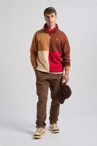 Persona che indossa una Color Block Quarter Zip Sweatshirt in Equestrian Red, con una miscela stilosa di colori tra cui rosso, marrone e beige, abbinata a pantaloni marroni e con un cappellino marrone in mano | TP_IMAGE_TYPE=MODEL_FRONT